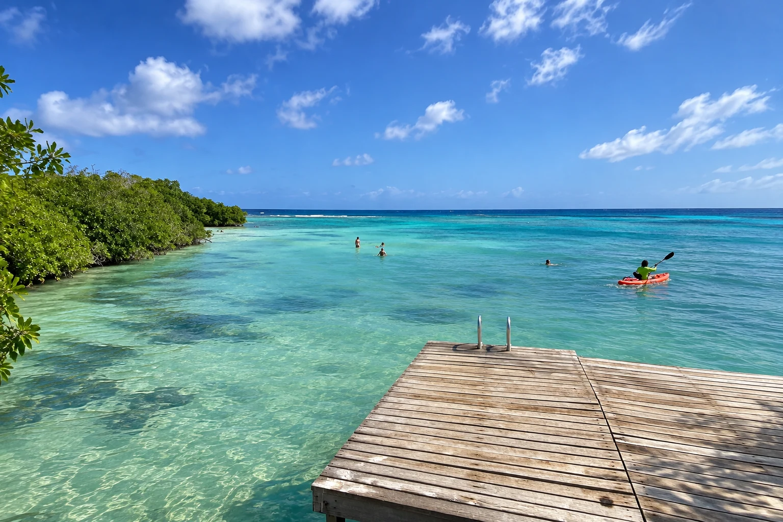 A wooden dock overlooking Mangel Halto’s mangroves and turquoise water, with a kayaker nearby