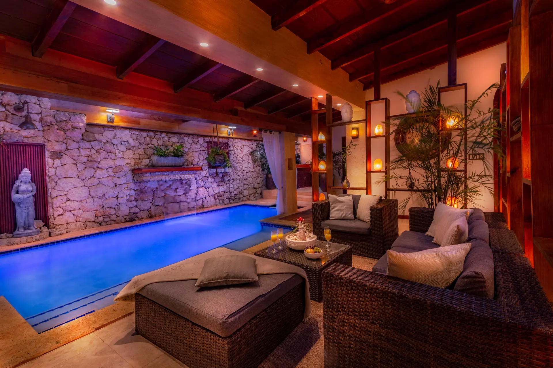 The indoor pool seen from the adjoining living room, with sofas overlooking the waterfall and Buddha statues