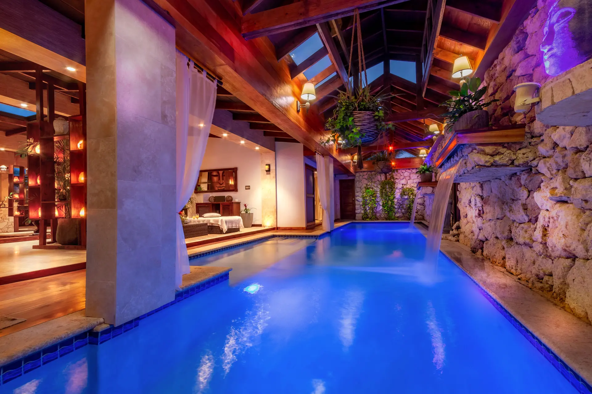 Bali Retreat’s indoor waterfall pool beneath a timber roof, beside a stone feature wall