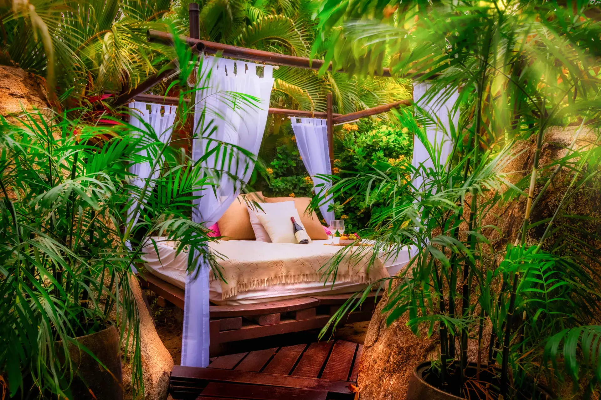 The Sky Bed surrounded by tropical greenery, white curtains and natural granite boulders at Bali Retreat Aruba